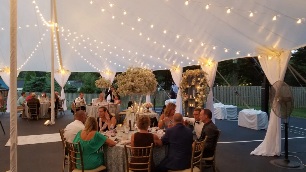 Wedding tent rental BC with guests seated at round tables under a 40x40 high top marquee tent with Gold Chiavari chairs”