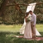 bride and groom posing in front of white draped adjustable backdrop at outdoor Kelowna wedding