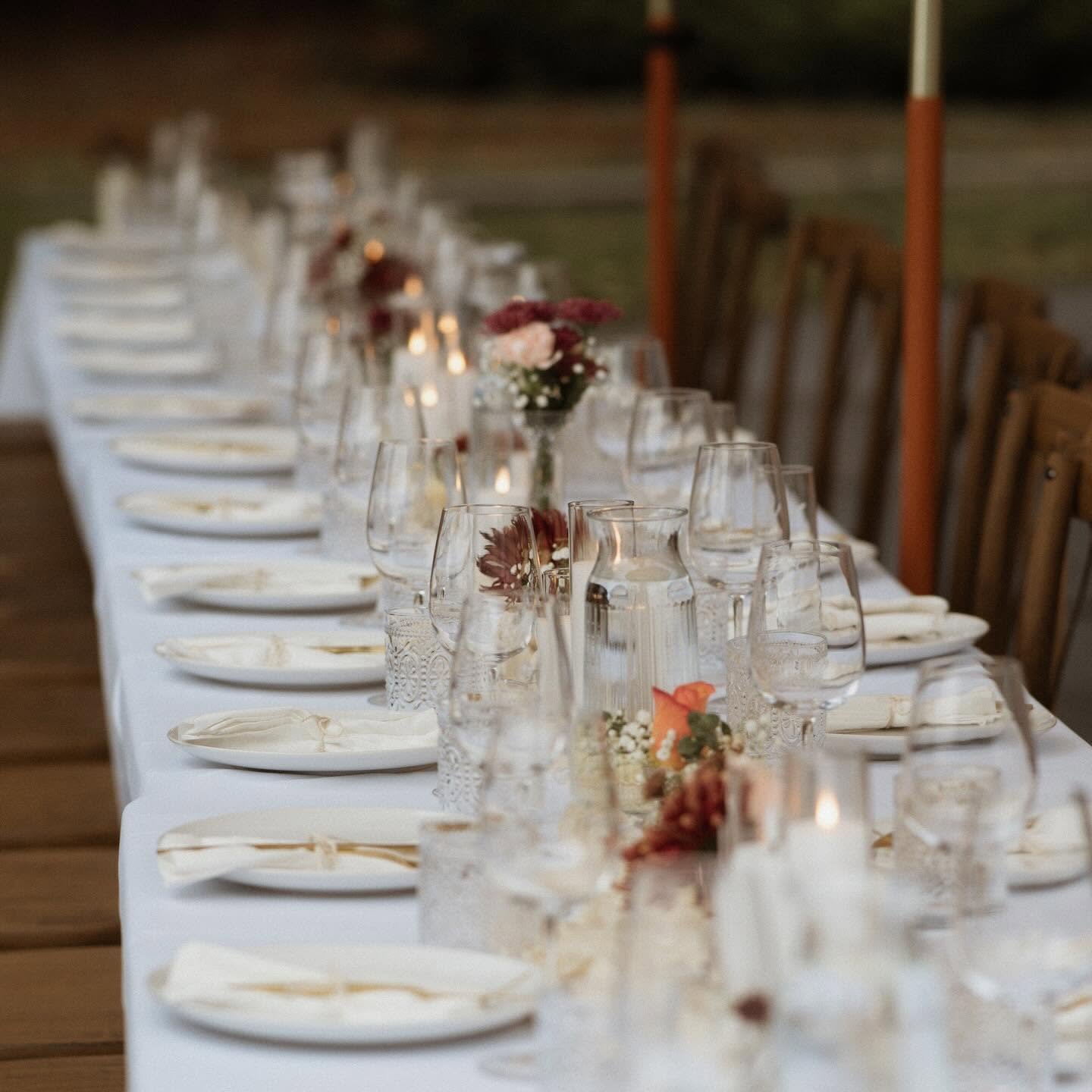 Elegant indoor dining table with white tablecloth, glassware, candles and small floral centrepieces