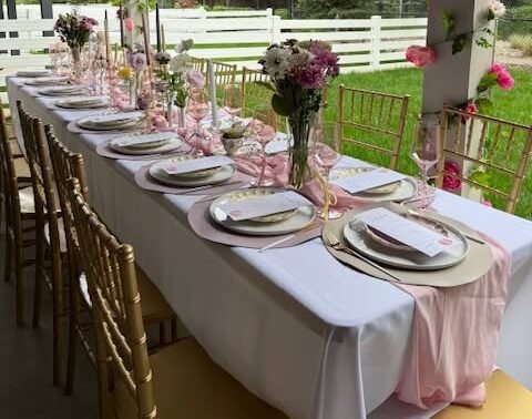 Outdoor banquet table with gold Chiavari chairs, white linens and pink floral decorations