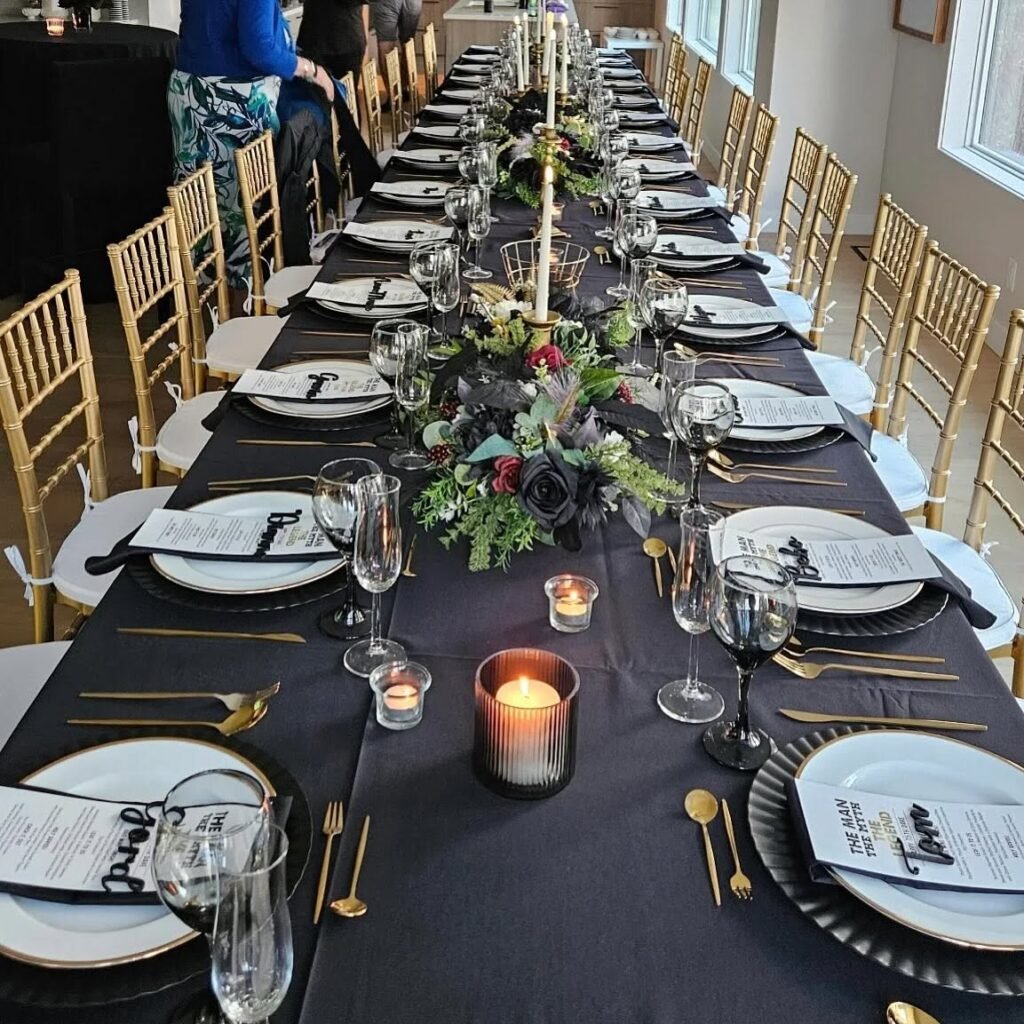 Indoor banquet table with black linens, gold Chiavari chairs, candles and floral centrepieces
