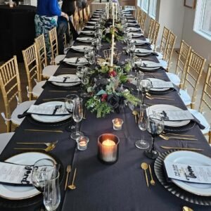 Indoor banquet table with black linens, gold Chiavari chairs, candles and floral centrepieces