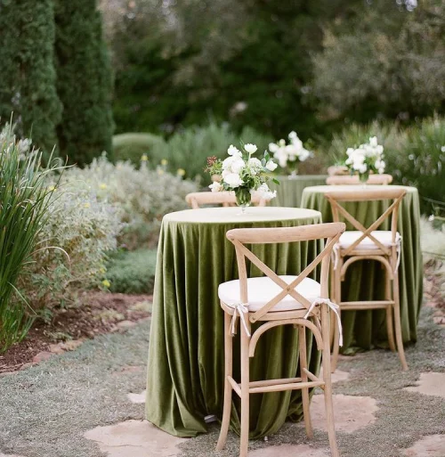 Low cocktail tables with olive green floor-length linens and wooden bar stools at an outdoor wedding venue